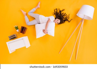 Full size high angle above flat lay view photo of beautiful little lady lying morning hug pillow comfy floor near book shelf lamp wear pajama isolated yellow color background