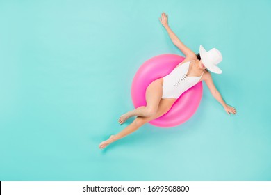 Full size high angle top above view photo of gentle lady spread arms taking sun bath sitting big life buoy swimming water wear sun hat white bodysuit isolated pastel teal color background