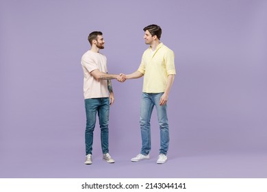 Full Size Length Two Young Smiling Happy Men Friends Together In Casual T-shirt Meeting Together Greeting Hold Hands Folded Handshake Gesture Isolated On Purple Background Studio Tattoo Translate Fun