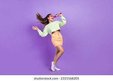 Full size photo of adorable pretty woman dressed green shirt stylish skirt sing in microphone on stage isolated on purple color background - Powered by Shutterstock