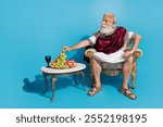 Full size photo of ancient leader prophet sit throne eat fresh grapes isolated on blue color background