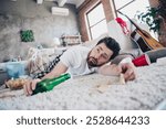 Full size photo of attractive young male lying floor drunk dressed sleepwear wake up after party day messy light home interior living room