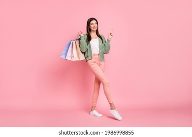 Full Size Photo Of Attractive Young Woman Look Point Finger Empty Space Hold Bags Isoalted On Pink Color Background