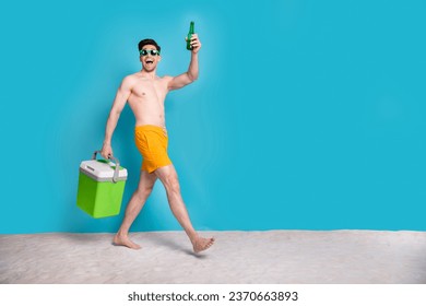 Full size photo of attractive young man walk hold beer bottle carry fridge wear trendy yellow shorts isolated on blue color background - Powered by Shutterstock