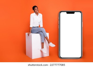 Full size photo of beautiful appearance female sitting podium near phone advertisement isolated on orange color background - Powered by Shutterstock