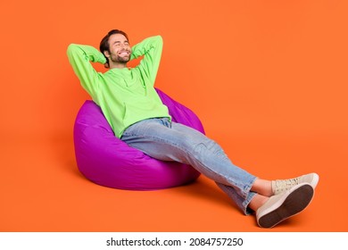 Full size photo of brunet millennial guy lie down sleep wear green sport cloth jeans shoes isolated on orange color background