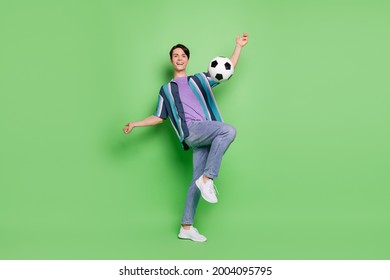 Full size photo of cheerful active joyful happy man kick football smile hobby game isolated on green color background - Shutterstock ID 2004095795