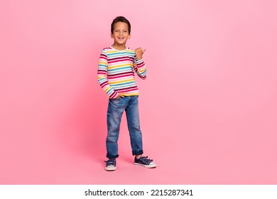 Full size photo of cheerful good mood boy wear striped shirt jeans arm in pocket directing empty space isolated on pink color background - Powered by Shutterstock