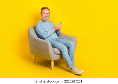 Full Size Photo Of Cheerful Man Sit Chair Hold Use Telephone Chatting Isolated On Yellow Color Background