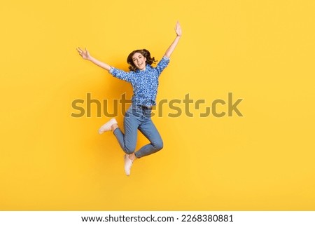 Full size photo of cheerful overjoyed girl jumping raise hands empty space isolated on yellow color background