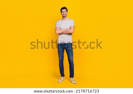 Full size photo of cool brunet young guy crossed arms wear t-shirt jeans sneakers isolated on yellow background