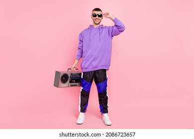 Full size photo of cool young brunet guy with boom box wear eyewear hoodie pants sneakers isolated on pink background - Shutterstock ID 2086723657
