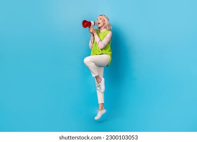 Full size photo of crazy excited girl hold loudspeaker talk empty space jumping isolated on blue color background