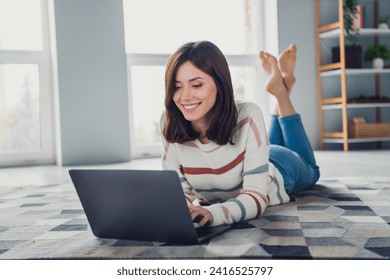 Full size photo of cute cheerful girl laying carpet floor use wireless laptop typing email living room house inside - Powered by Shutterstock