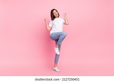 Full size photo of ecstatic girl raise fist in victory triumph wear denim white sneakers isolated on pink color background