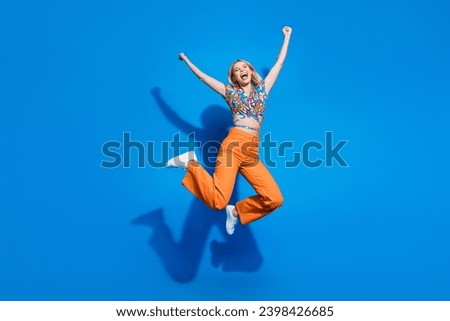 Full size photo of ecstatic optimistic girl wear blouse orange trousers jumping hands up win betting isolated on blue color background