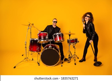 Full size photo of famous rock group guy plays instruments beat drum, sticks attractive girl sings mic night club performance show concert wear black leather outfit isolated yellow background