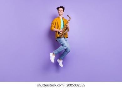Full size photo of funky brunet millennial guy jump with sax wear shirt jeans isolated on violet color background