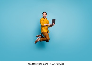 Full size photo of funky man feel rejoice emotions jump use laptop search social media online black friday discounts wear casual style clothing isolated over blue color background