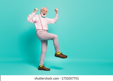 Full Size Photo Of Funny Excited Grandpa Raise Fists Leg Celebrate Senior Meeting Party Wear Specs Pink Shirt Suspenders Bow Tie Pants Shoes Yellow Socks Isolated Teal Color Background