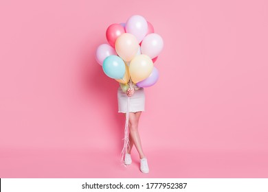 Full Size Photo Of Funny Lady Come Birthday Party Hold Many Air Balloons Hiding Face Surprise Visit Wear Casual Green Crop Pullover Jeans Skirt Shoes Isolated Pink Pastel Color Background