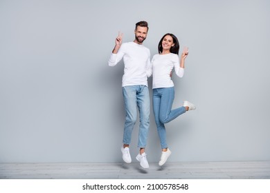Full size photo of funny millennial brunet couple jump wear white shirt jeans sneakers isolated on grey background