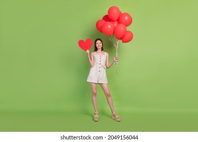 Full size photo of funny young brunette lady hold heart balloons wear overall sandals isolated on green background