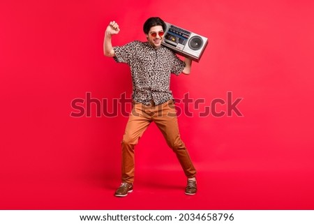Full size photo of good mood smiling handsome male dancing with boombox summer weekend isolated on red color background