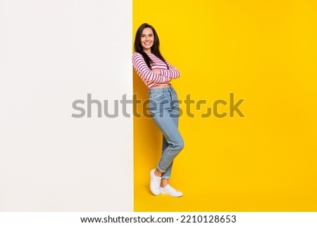 Full size photo of good mood nice girl wear striped shirt jeans leaning on white wall empty space isolated on yellow color background