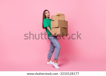 Full size photo of gorgeous nice cute girl with long hairstyle wear green t-shirt jeans hold heavy boxes isolated on pink color background