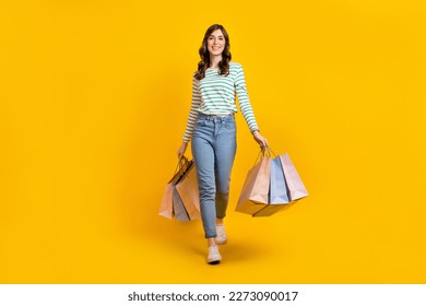 Full size photo of gorgeous woman with curly hairstyle striped denim pants hold bags go shopping isolated on yellow color background