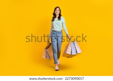 Full size photo of gorgeous woman with curly hairstyle striped denim pants hold bags go shopping isolated on yellow color background
