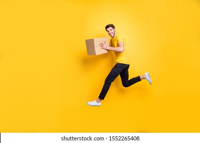 Full Size Photo Of Handsome Guy Jumping High Holding Parcel Box Hurry Move New Apartments Transportation Wear Casual T-shirt Pants Isolated Yellow Color Background