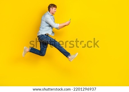 Full size photo of handsome guy red hair blue shirt jeans sneakers chatting listen notification online isolated on yellow color background