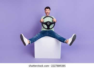 Full size photo of handsome man sit white cube hold steering wheel crazy dressed stylish gray look isolated on purple color background