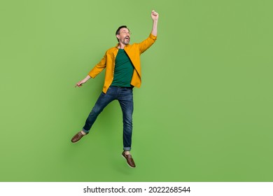 Full size photo of handsome mature man happy positive smile try to catch umbrella jump isolated over green color background - Shutterstock ID 2022268544