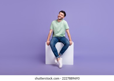 Full size photo of handsome young man sitting white podium look empty space dressed stylish gray outfit isolated on purple color background