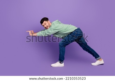 Full size photo of handsome young man pushing heavy empty space dressed stylish khaki garment isolated on purple color background