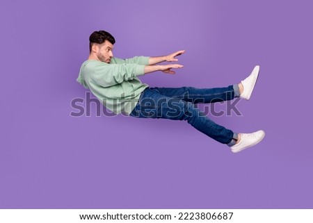 Full size photo of handsome young man flying away strong wind blow push dressed stylish khaki clothes isolated on purple color background