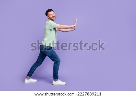 Full size photo of handsome young man pushing empty space wall cheerful dressed stylish gray garment isolated on purple color background