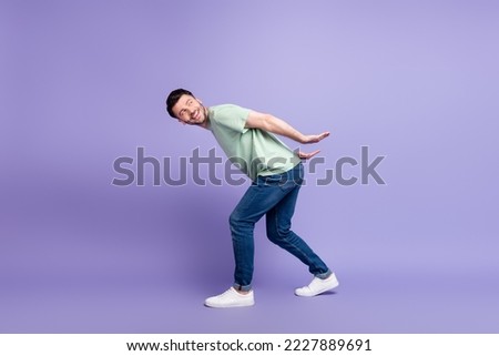 Full size photo of handsome young guy carry back look empty space invisible box wear trendy gray outfit isolated on violet color background