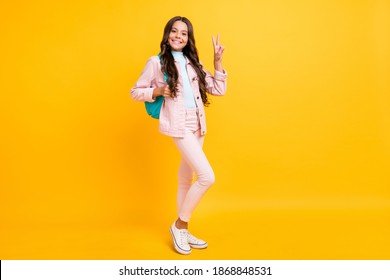 Full size photo of happy charming girl make v-sign wear pink jacket pants backpack isolated on yellow color background