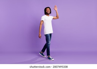 Full Size Photo Of Happy Dark Skin Young Man Walk Wave Hand Hello Free Time Isolated On Purple Color Background