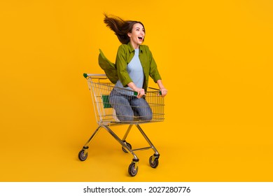 Full size photo of happy nice young woman look empty space ride trolley isolated on yellow color background