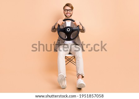 Full size photo of happy positive good mood handsome man riding car hold steering wheel isolated on beige color background