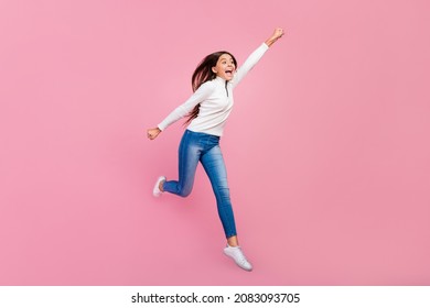 Full size photo of impressed brunette teen supergirl jump wear sweater jeans footwear isolated on pink color background