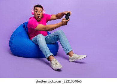 Full size photo of impressed gamer person sit comfy bag hold controller play games isolated on violet color background