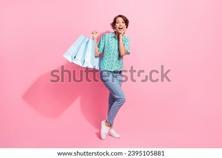 Full size photo of impressed positive girl hold shop bags hand touch cheek isolated on pink color background