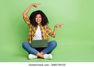 Full Size Photo Of Impressed Wavy Hairstyle Young Lady Sit With Laptop Indicatte Promo Wear Spectacles Shirt Jeans Sneakers Isolated On Green Background