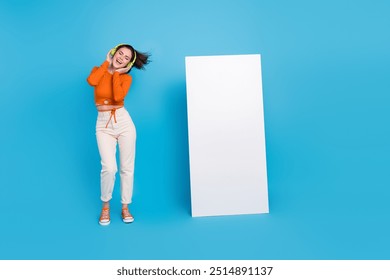 Full size photo of impressed young brunette lady wear headphones shirt trousers sneakers isolated on blue background - Powered by Shutterstock